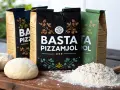 Tre påsar BASTA Pizzamjöl står uppradade. Framför dem ligger en degboll och en hög mjöl med en träsked. Perfekt för hemmagjord pizza!