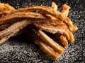 En hög med gyllene churros españoles, pudrade med socker, ligger på en mörk yta.