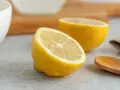 Två halvor av en saftig citron ligger på en grå yta. En träsked ligger bredvid. Perfekt för att pressa ut lite jugo de limón.