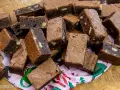 En hög med saftiga, hembakade pasteles de chocolate, vissa med nötter, ligger på ett mönstrat papper.
