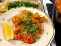 En tallrik med kyckling och ris, kryddad med paprika och persilja. En citronklyfta ligger bredvid. En gryta med samma rätt syns i bakgrunden.