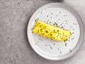 En perfekt rullad omelett, strödd med gräslök, på en tallrik. Enkel guide för como hacer un omelet.