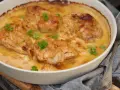 En ugnsform med saftig pollo encebollado salvadoreño, kyckling i en krämig löksås, garnerad med persilja.