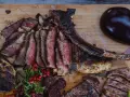 En saftig tomahawk steak, skuren i skivor, serveras med grillad aubergine, potatis i folie och lingon.