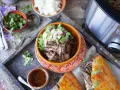 En skål med saftig, långkokt högrev (birria de res) toppad med lök och koriander. Serveras med en liten skål med sås och en gyllene quesadilla.