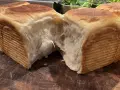 Mjukt och fluffigt **pan de leche** som brutits isär på en träskärbräda. Den gyllene skorpan kontrasterar mot det vita, trådiga inkråmet.