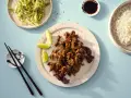 Krispiga chicharrones de cerdo med sesamfrön, serverade med ris, sallad och limeklyftor.