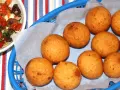 Gylla gyllenbruna friterade bollar, som visar hur man gör buñuelos, i en blå korg. Bredvid en skål med en färgglad sallad.