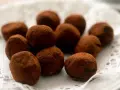 En hög med chokladtryfflar, pudrade med kakao, ligger på en vit spetsduk.