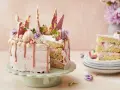 En rosa tårta med jordgubbsfrosting, chokladdekorationer och färska bär. En bit av tårtan visas på en stapel tallrikar.