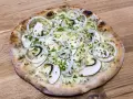 En pizza de hongos med tunna skivor champinjoner, lökringar och gräslök på en träbakgrund.