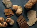 En variation av olika tipos de pan: mörkt rågbröd, knäckebröd, surdegsbröd och frallor.