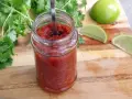 En burk med hemlagad salsa para tacos, med färsk koriander och limeklyftor på en träskärbräda.