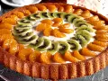 En vacker tartaleta de frutas med mandarinklyftor och kiwiskivor arrangerade i ett mönster på en krämig fyllning.