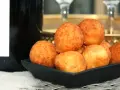 En svart skål fylld med gyllene pan de queso, bredvid en flaska champagne. Perfekt för en festlig stund.