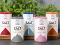 Fem olika tipos de sal från Falksalt: finkornigt, bergsalt, havssalt, Himalaya och jodberikat. Gröna örter i bakgrunden.