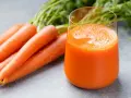 Färskt morotsjuice i ett glas, bredvid en hög med morötter. Morotsjuice är bra för synen och immunförsvaret.