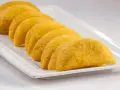 En rad gyllene empanadas de plátano ligger på en vit rektangulär bricka.