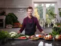 En kock i köket med ett överflöd av färska grönsaker, redo att visa olika tipos de cortes de vegetales.