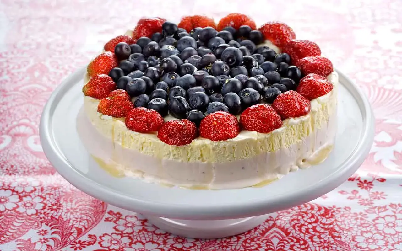 En vacker pastel de cumpleaños, toppad med färska jordgubbar och blåbär, ser utsökt ut på ett vitt tårtfat.