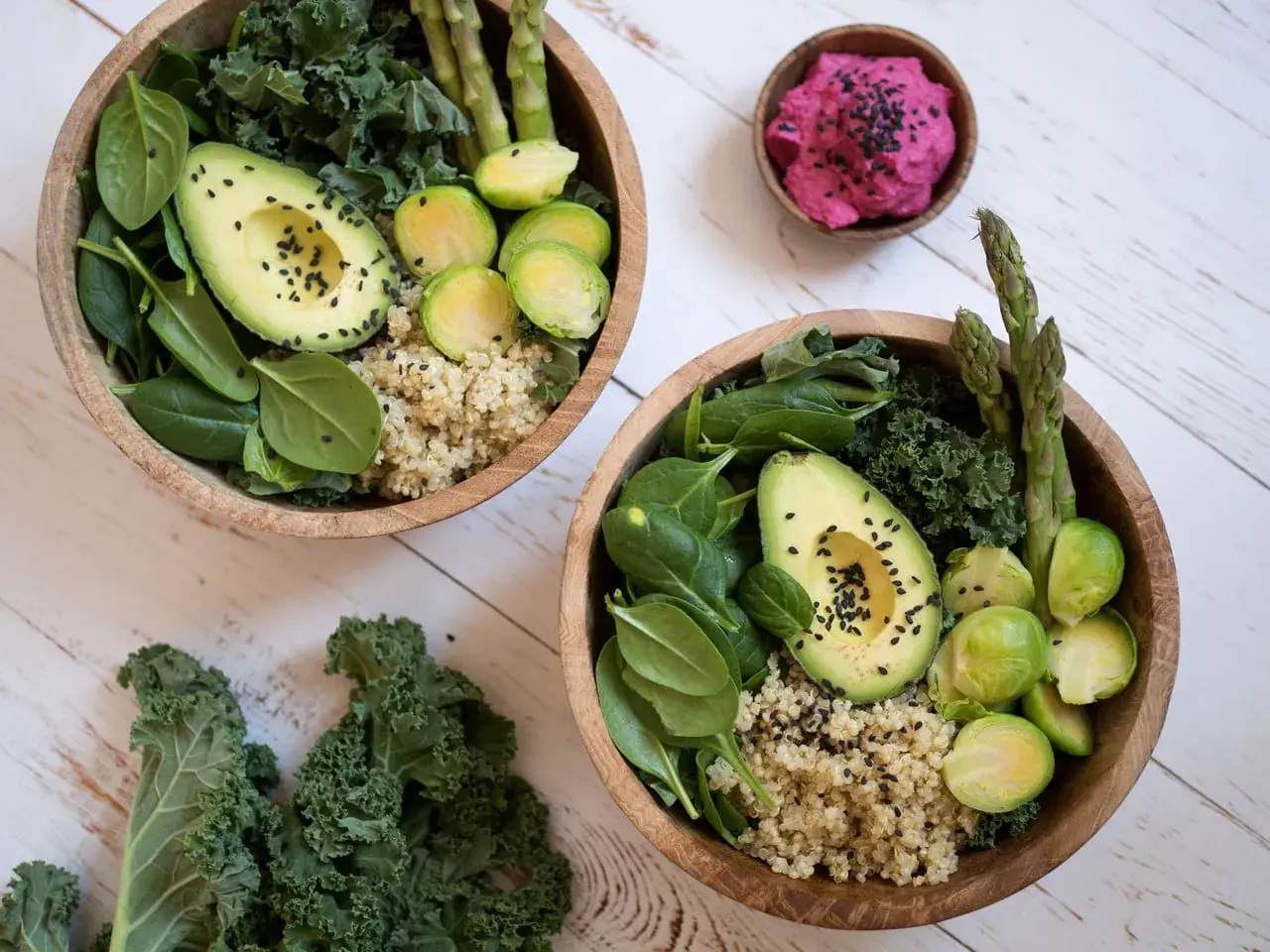 Två skålar med quinoa, spenat, grönkål, avokado, brysselkål och sparris. En liten skål med rosa röra. Perfekt för en **comida saludable**.