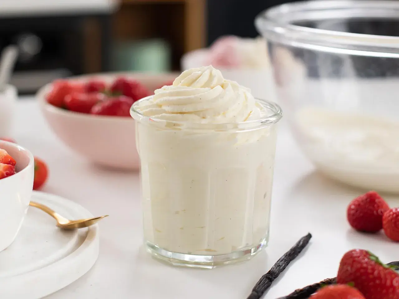 En krämig crema chantilly i ett glas, omgiven av färska jordgubbar och vaniljstänger. Perfekt för sommardesserter.