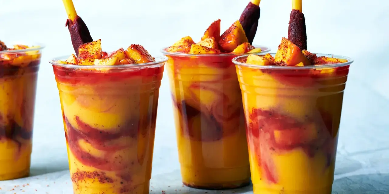 Färgglada mangodrycker med chili och fruktbitar. En perfekt guide för como hacer mangoneadas!