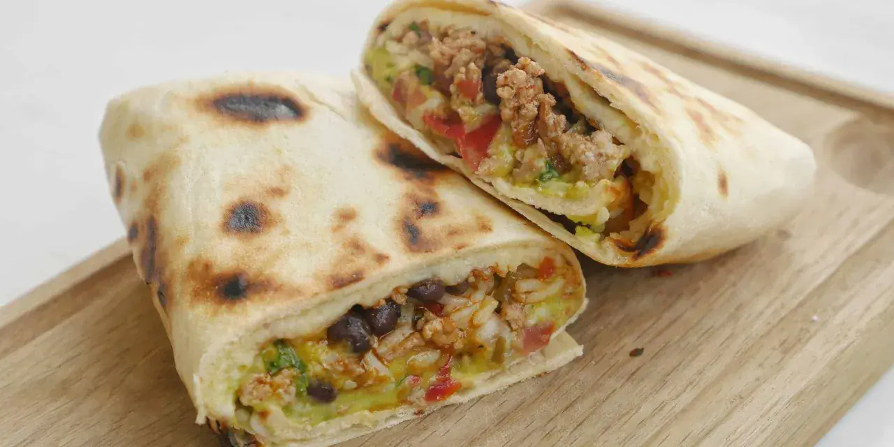 Två halverade burritos de carne med köttfärs, bönor, ris och grönsaker på en träskärbräda.