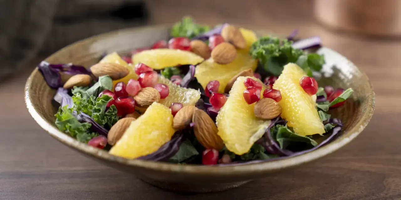 En färgstark sallad med apelsinklyftor, granatäppelkärnor, mandlar och olika typer av lechuga som grönkål och rödkål.