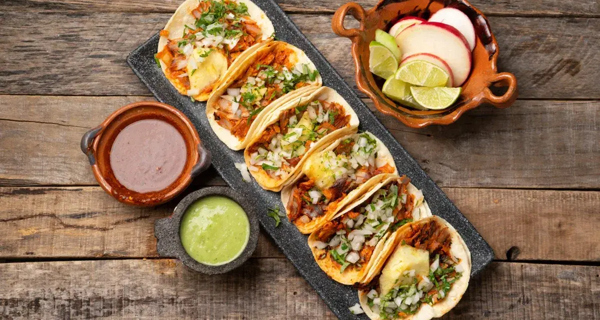 Tacos al pastor med saftig fläskkött, ananas, lök och koriander. Serveras med salsa verde, bönor och lime.