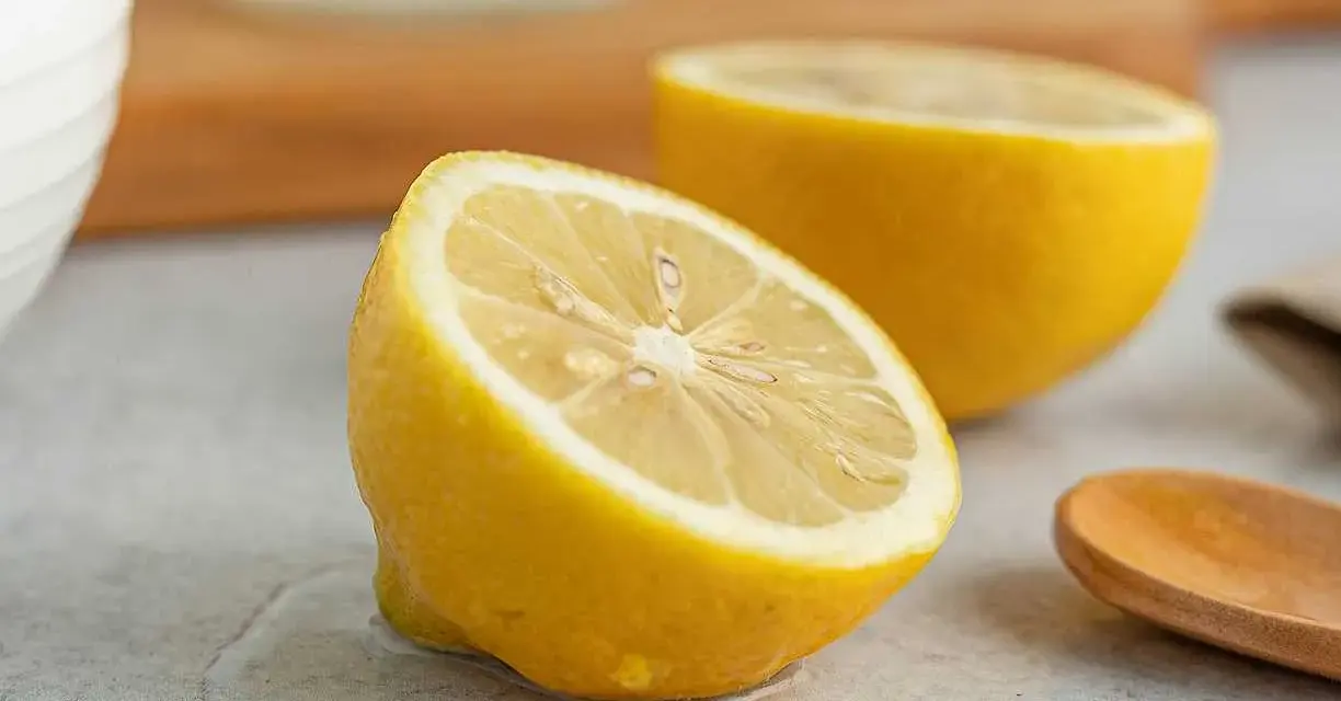 Två halvor av en saftig citron ligger på en grå yta. En träsked ligger bredvid. Perfekt för att pressa ut lite jugo de limón.