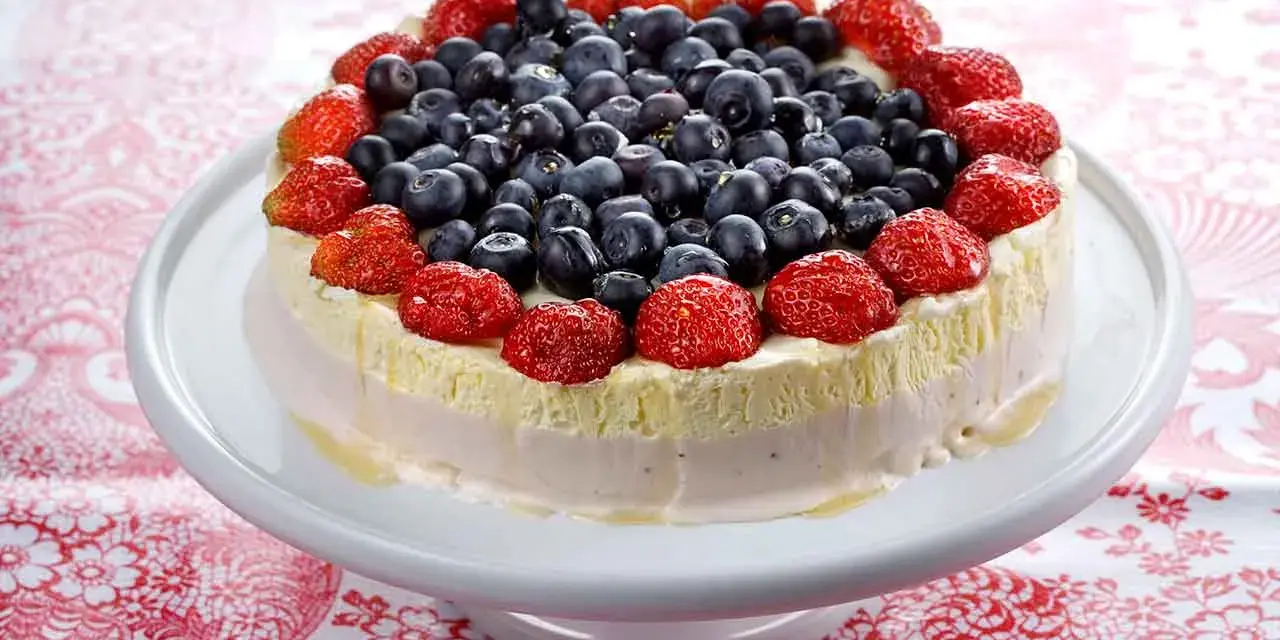 En vacker pastel de cumpleaños, toppad med färska jordgubbar och blåbär, ser utsökt ut på ett vitt tårtfat.