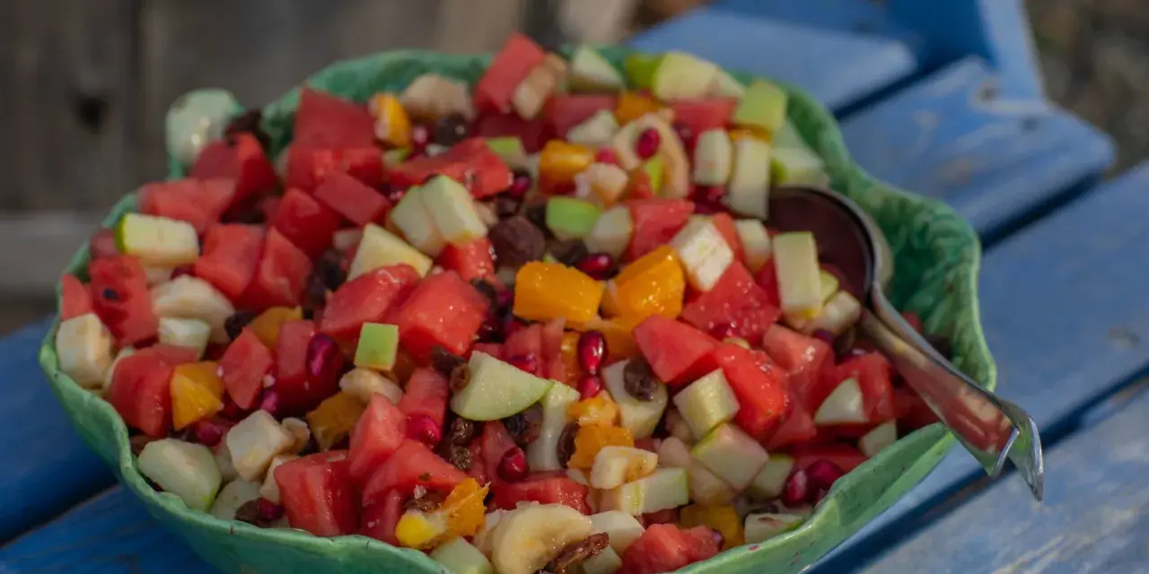 En stor skål med en färgglad ensalada de frutas, fylld med vattenmelon, äpple, apelsin, banan och granatäpple.