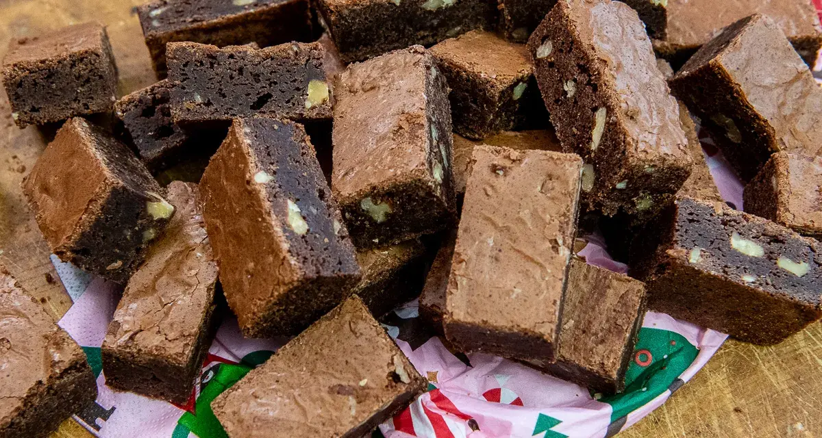 En hög med saftiga, hembakade pasteles de chocolate, vissa med nötter, ligger på ett mönstrat papper.