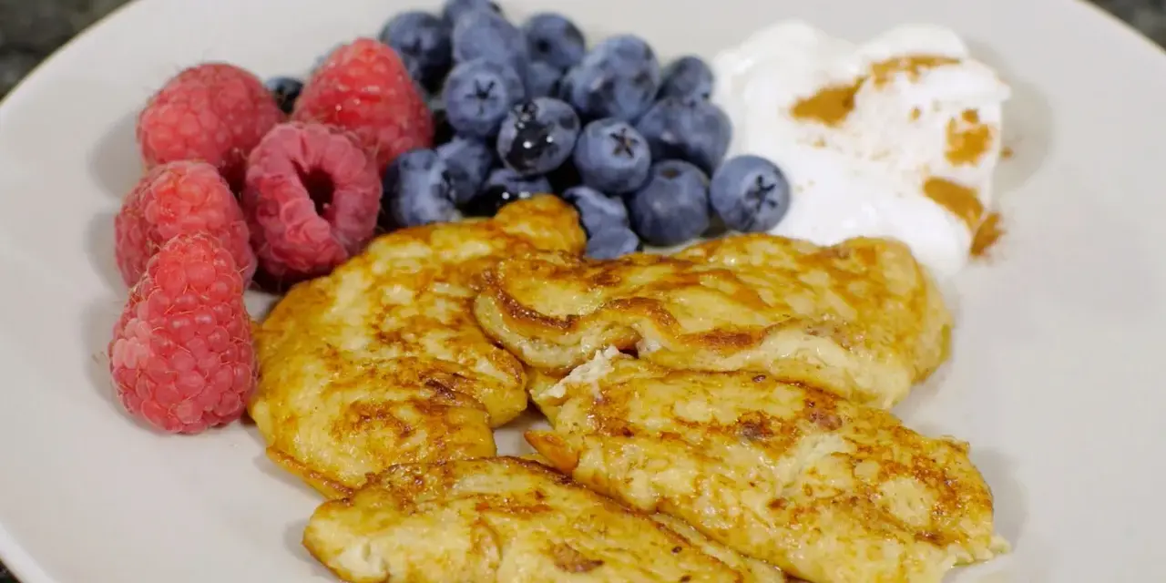En tallrik med gyllene pannkakor, färska hallon, blåbär och en klick yoghurt med kanel. Perfekt för cenas para diabeticos.
