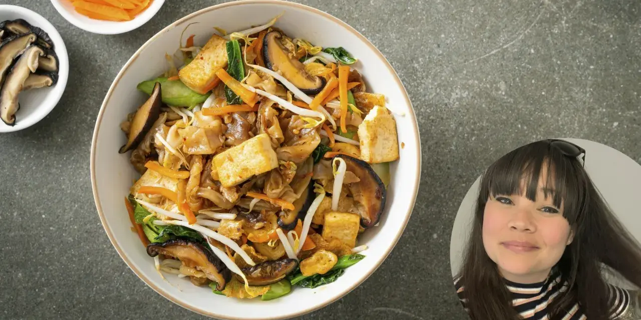 En skål med nudlar, tofu, svamp och grönsaker. En kvinna ler i ett hörn.