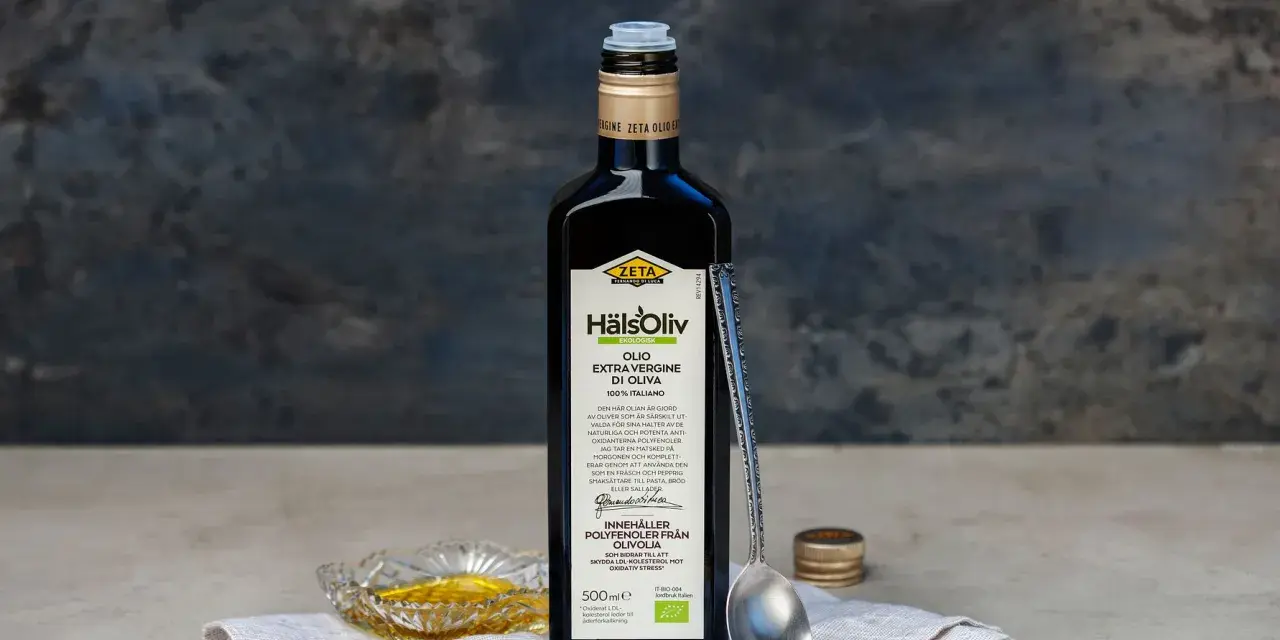 En flaska Zeta Hälsoliv Ekologisk Olio Extra Vergine di Oliva, perfekt aceite de oliva para cocinar. En sked och en liten skål med olja syns också.