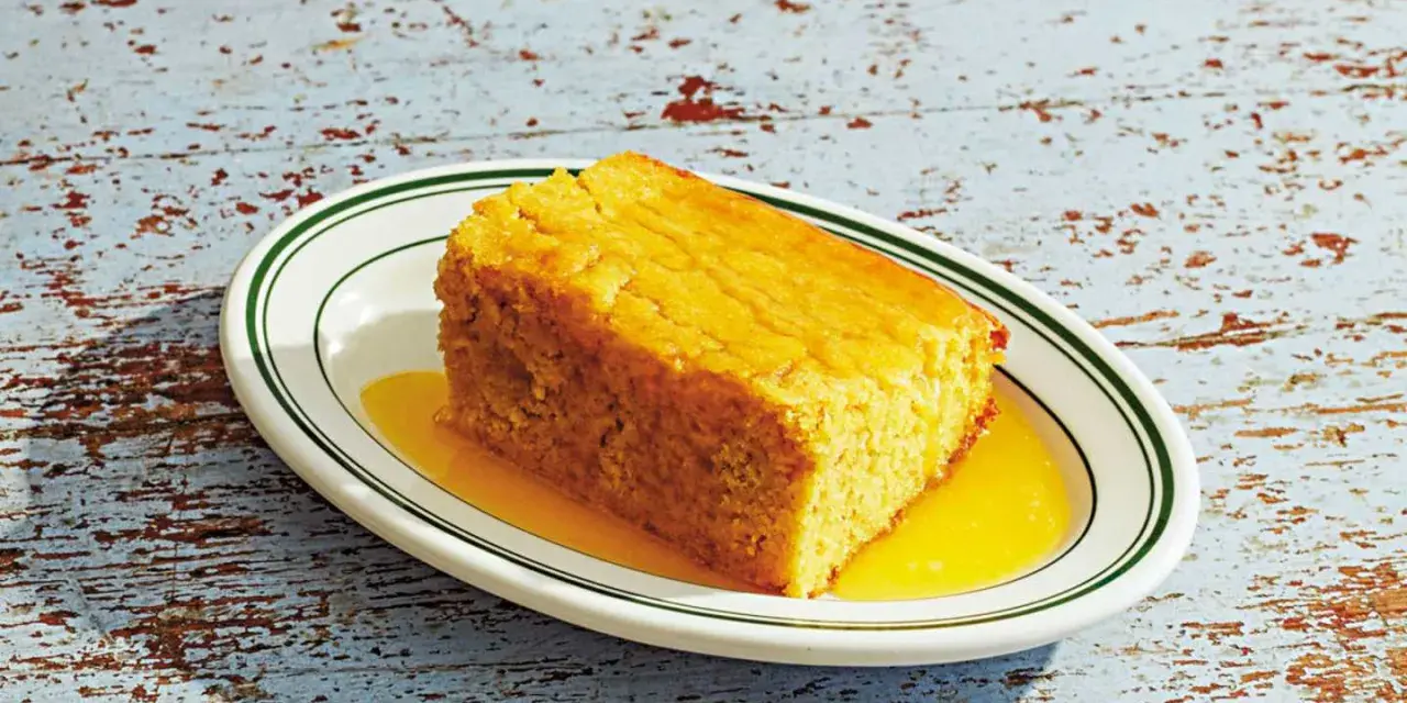 En bit gyllene pan de maiz, saftig och serverad med en gyllene sirap på en vit tallrik med gröna kanter.