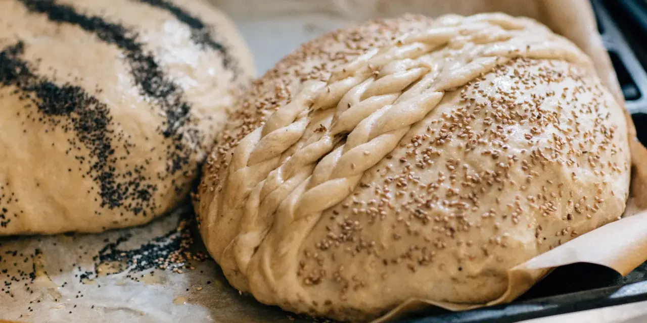Två olika tipos de pan dulce, en med vallmofrön och en flätad med sesamfrön, redo att bakas.