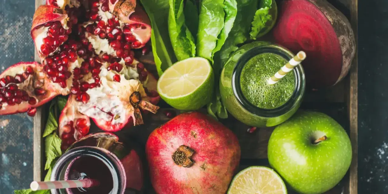 En låda med färska frukter och grönsaker, inklusive granatäpplen, äpplen, lime, rödbetor och gröna smoothies. Perfekt för naturliga botemedel mot gastrit.