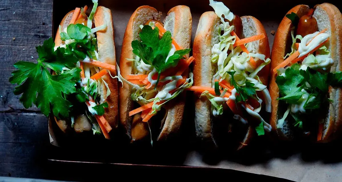 Fyra läckra korv med bröd, toppade med krispig kål, morötter och persilja. Enkel guide: como hacer un hot dog.