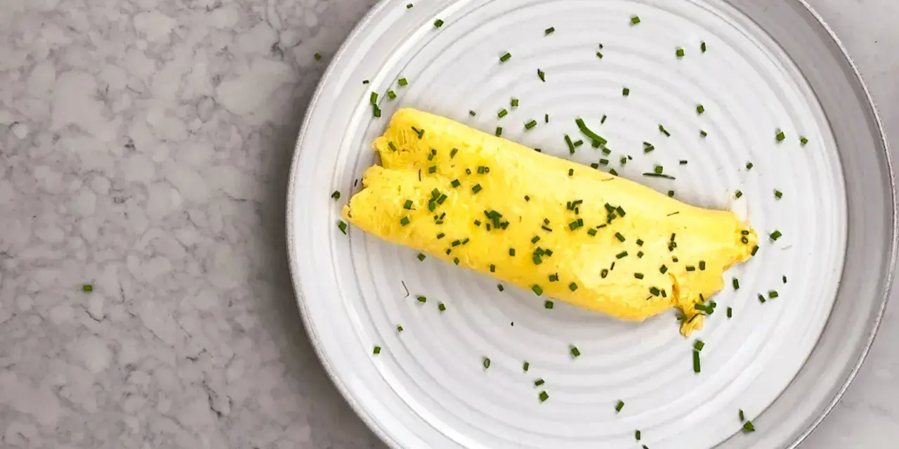 En perfekt rullad omelett, strödd med gräslök, på en tallrik. Enkel guide för como hacer un omelet.