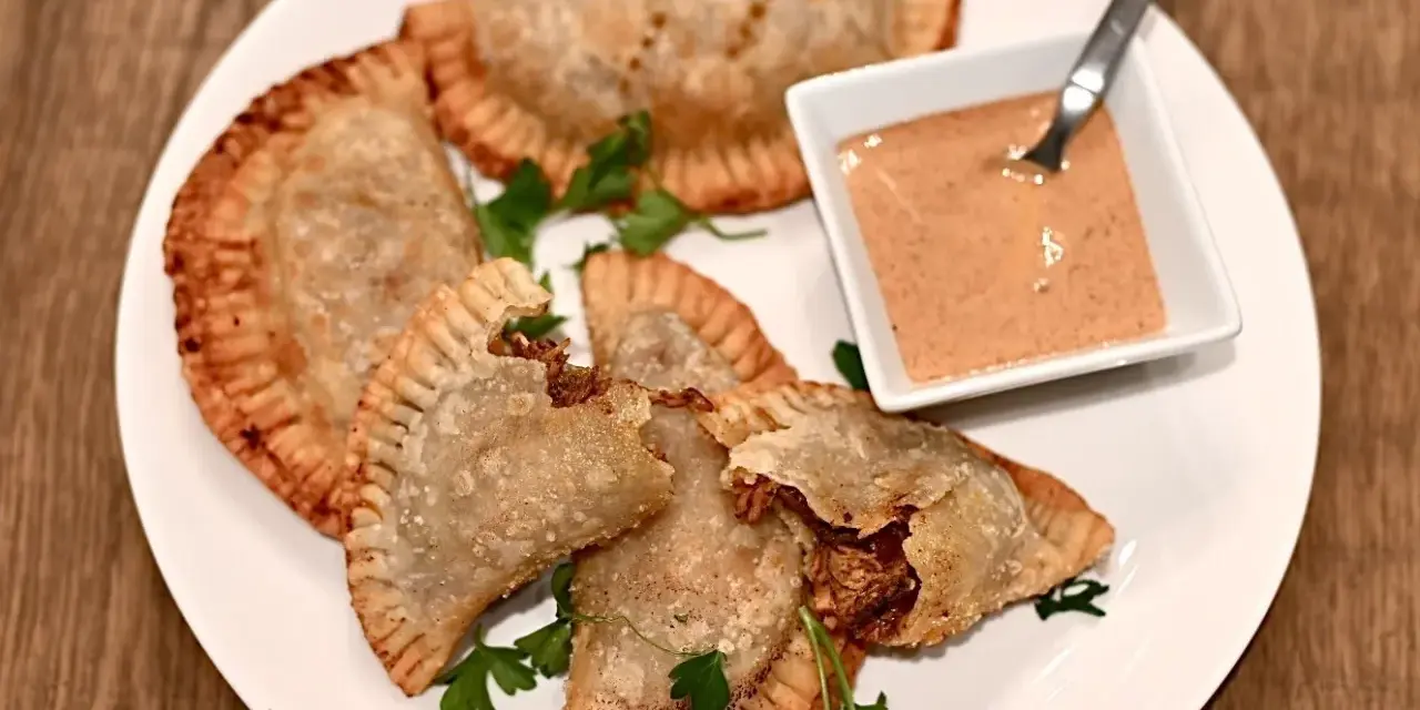 Friterade pastelitos de pollo med en krämig dippsås och persilja på en vit tallrik.