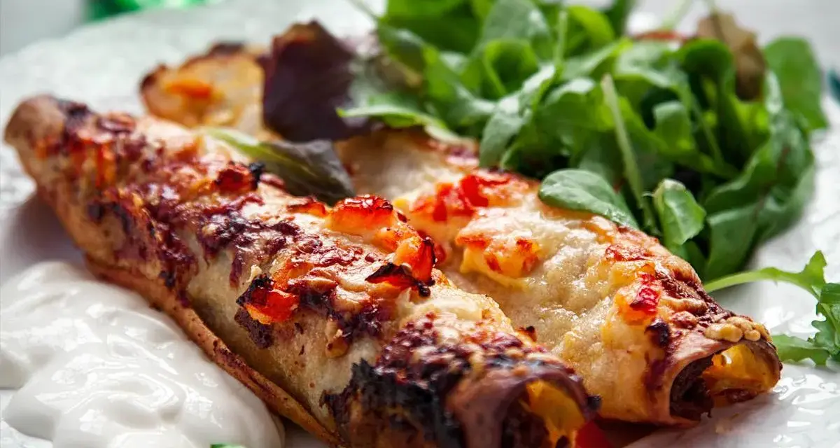 Två gyllene enchiladas, en typisk maträtt från Guatemala, serveras med en fräsch sallad och en klick gräddfil.