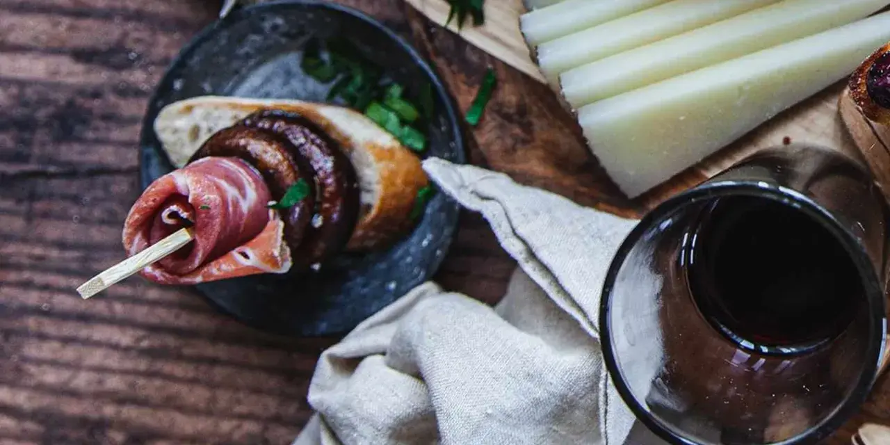 En läcker pinchos de carne med prosciutto, bröd och en skiva korv, serverad med ost och rödvin.