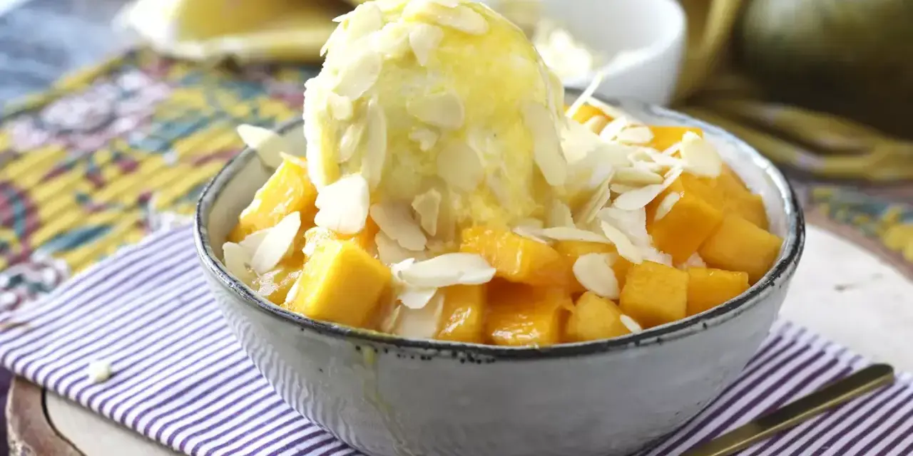 En skål med tärnad mango och en kula vaniljglass, toppad med mandelflagor. En härlig mango en miel-dessert.