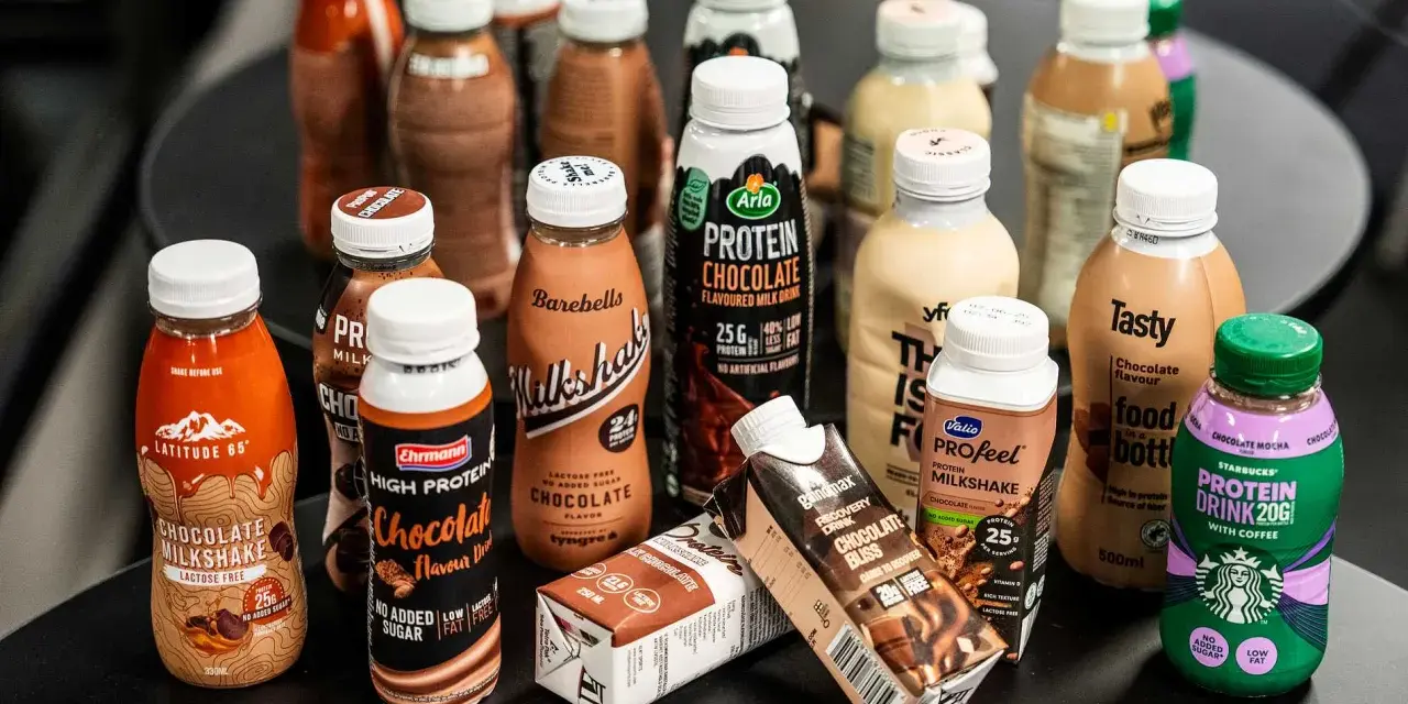 En samling flaskor och kartonger med olika sorters batido de proteinas, mestadels chokladsmak.