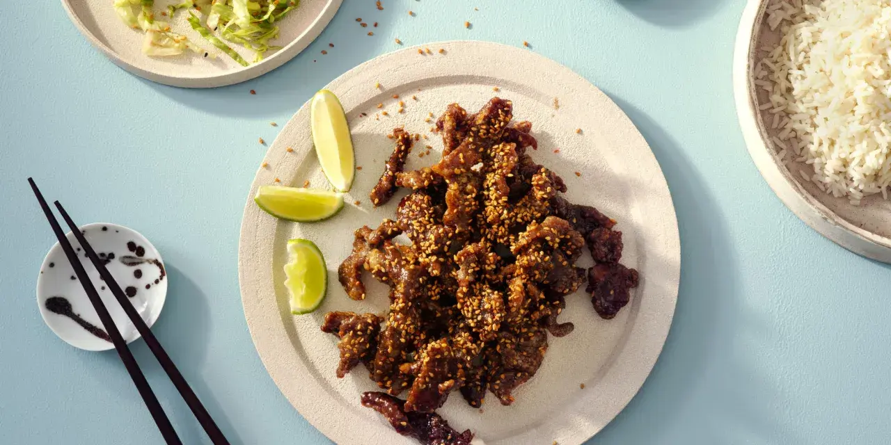 Krispiga chicharrones de cerdo med sesamfrön, serverade med ris, sallad och limeklyftor.