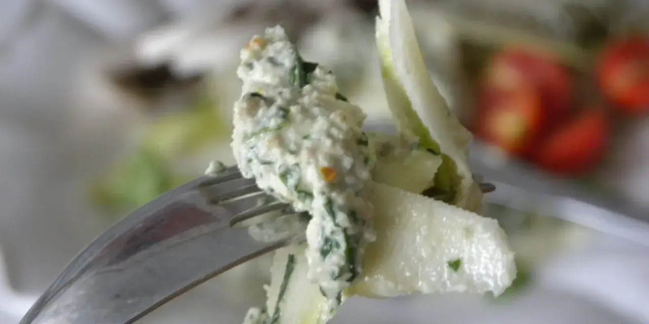 En gaffel med en krämig sallad, kanske med inslag av papayakärnor, nära körsbärstomater.