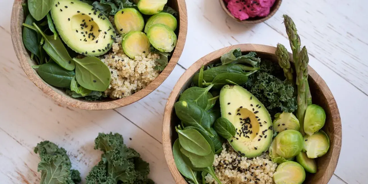 Två skålar med quinoa, spenat, grönkål, avokado, brysselkål och sparris. En liten skål med rosa röra. Perfekt för en **comida saludable**.